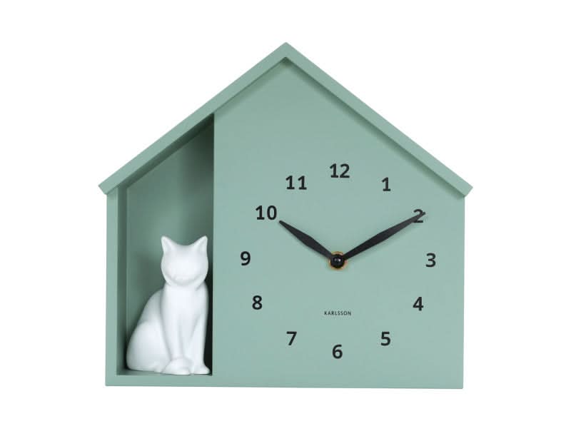 Hausförmige Wanduhr in Mintgrün mit sitzender weißer Katze, Ziffern 1–12 und schwarzen Zeigern