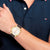 Tommy Hilfiger Herren-Armbanduhr am Handgelenk: weißes Zifferblatt, dunkles Lederband, goldene Lünette.