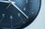 Nahaufnahme von Ziffern und Zeigern einer dunkelblauen Wanduhr am schwarzen Rand