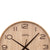 AMS-Wanduhr im Detail: Naturholz-Zifferblatt, schwarze Ziffern 10–3 und Zeigerkreuz.