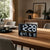 Digital table clock with LED display in black, shows time and temperature/humidity.