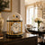 Gold-colored table clock with glass dome on sideboard, white dial with Roman numerals