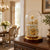 Table clock under glass dome on wooden table, gold dial with Roman numerals