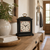 Black table clock on wooden surface, white dial with floral frame, gold handle
