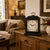 Black table clock with wooden case, gold-colored carrying handle, and floral pattern on the dial
