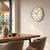 Wall clock on the wall in the living room: beige dial with black hands in a wooden frame.