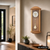 Wanduhr aus hellem Holz mit Pendel, rundem Zifferblatt und Glasfront
