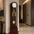 Grandfather clock with dark wood casing, white dial, and gold-colored pendulum behind glass