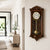 Dark wood wall clock with glass front, gold pendulum, and white dial