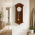 Wooden wall clock made of dark wood with a clock face and golden pendulum behind glass.