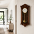 Braune Holz-Wanduhr an der Wand mit rundem Zifferblatt und goldfarbener Glocke