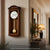 Wanduhr aus Holz mit rundem Zifferblatt, schmaler Front und Pendelgewicht-Optik