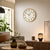 Wall clock on the wall above living room furniture, beige dial with black hands in a wooden frame.