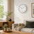 Wall clock on wall above sofa, round white dial with black numbers and hands