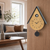Cuckoo clock on wood paneling, gold dial, black sides, and round pendulum weight