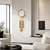 Gold-colored wall clock with decorative pendulums on a white wall