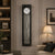Wall clock with black frame, round dial, and metal pendulum in glass