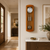 Wooden wall clock on the wall with a round dial, glass, and metal pendulum