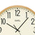 Wall clock dial in detail: beige face, black 12 and hands, light wood frame.