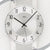 Nahaufnahme Wanduhr: weißes Zifferblatt mit AMS-Logo, schwarze Zeiger, Facettenring