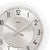Nahaufnahme Wanduhr: silbernes Zifferblatt mit AMS-Logo, schwarze Zahlen und Zeiger