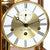 Close-up of the table clock: golden movement, white dial with Roman hour markers