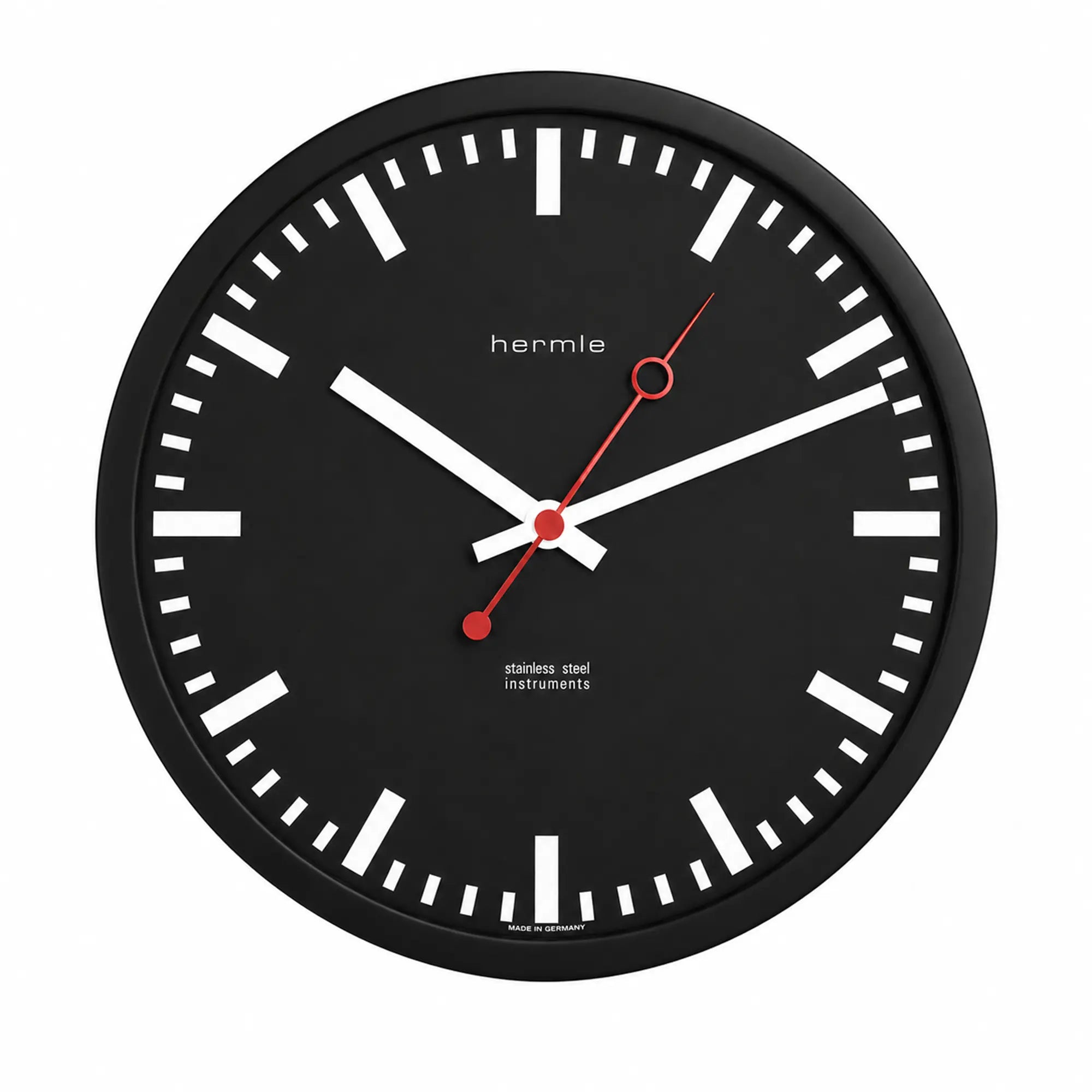 Round wall clock with black dial, white hour markers, and red hands